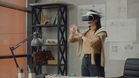 Female-engineer-in-the-office-in-a-virtual-reality-helmet-uses-gestures-to-manage-the-project-without-leaving-the-office.-Construction-control.-Design-project-of-the-building-and-interior